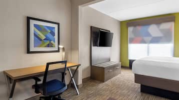 Habitación de hotel con cama, escritorio, silla, televisor y un cuadro en la pared.