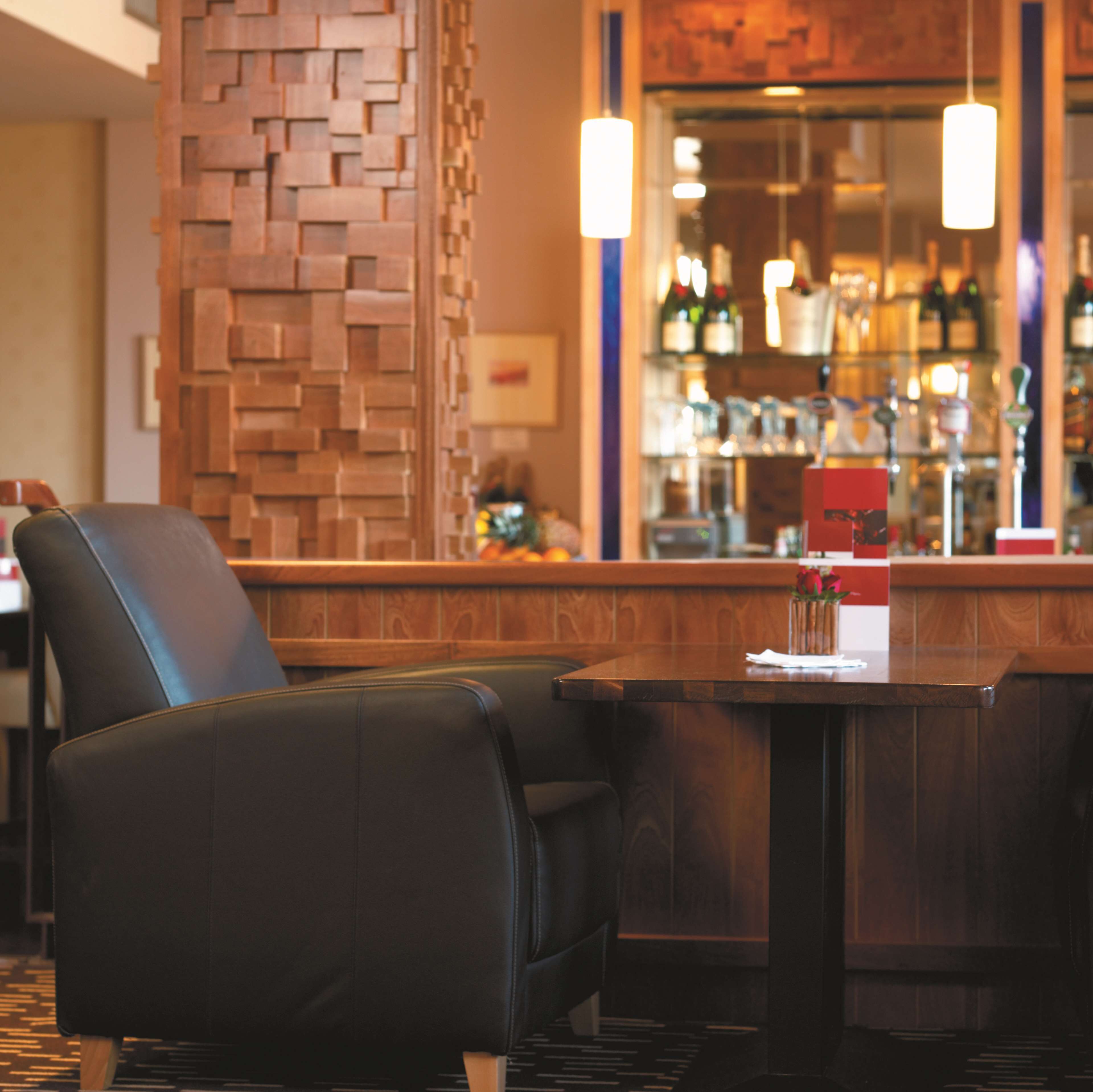 A bar area with a wooden wall, bar stools, and a counter with bottles.