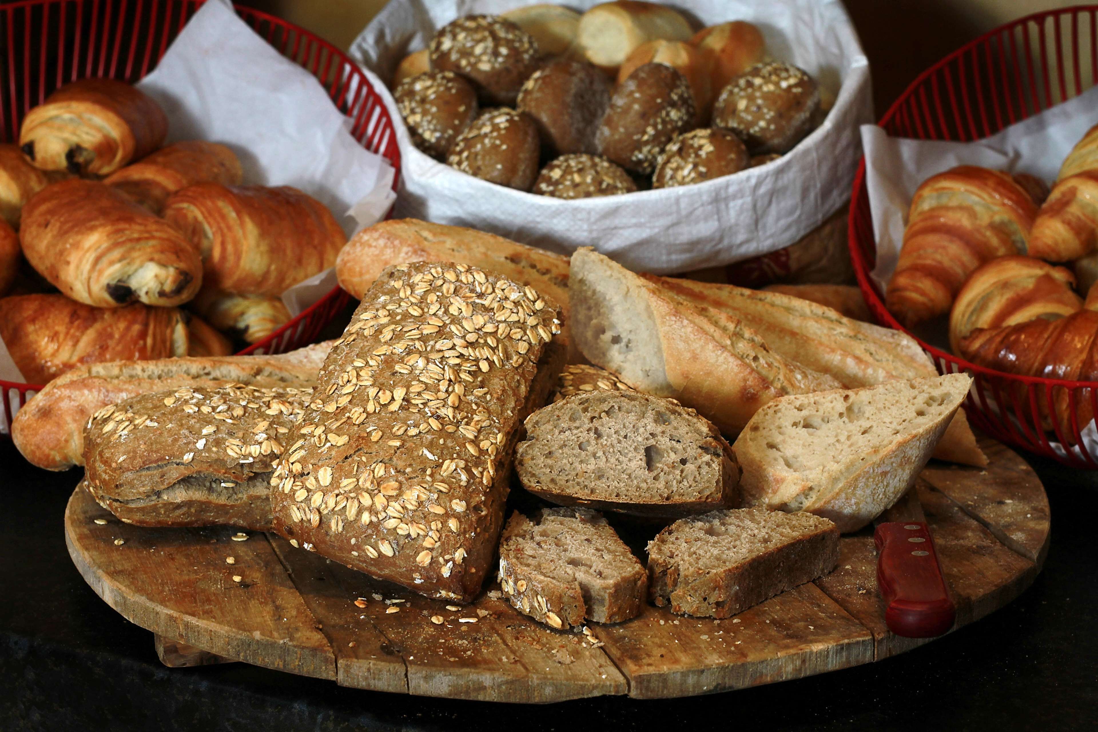 A variety of breads and pastries on a wooden board, including whole and sliced loaves, with baskets in the background.