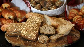 A variety of breads and pastries on a wooden board, including whole and sliced loaves, with baskets in the background.