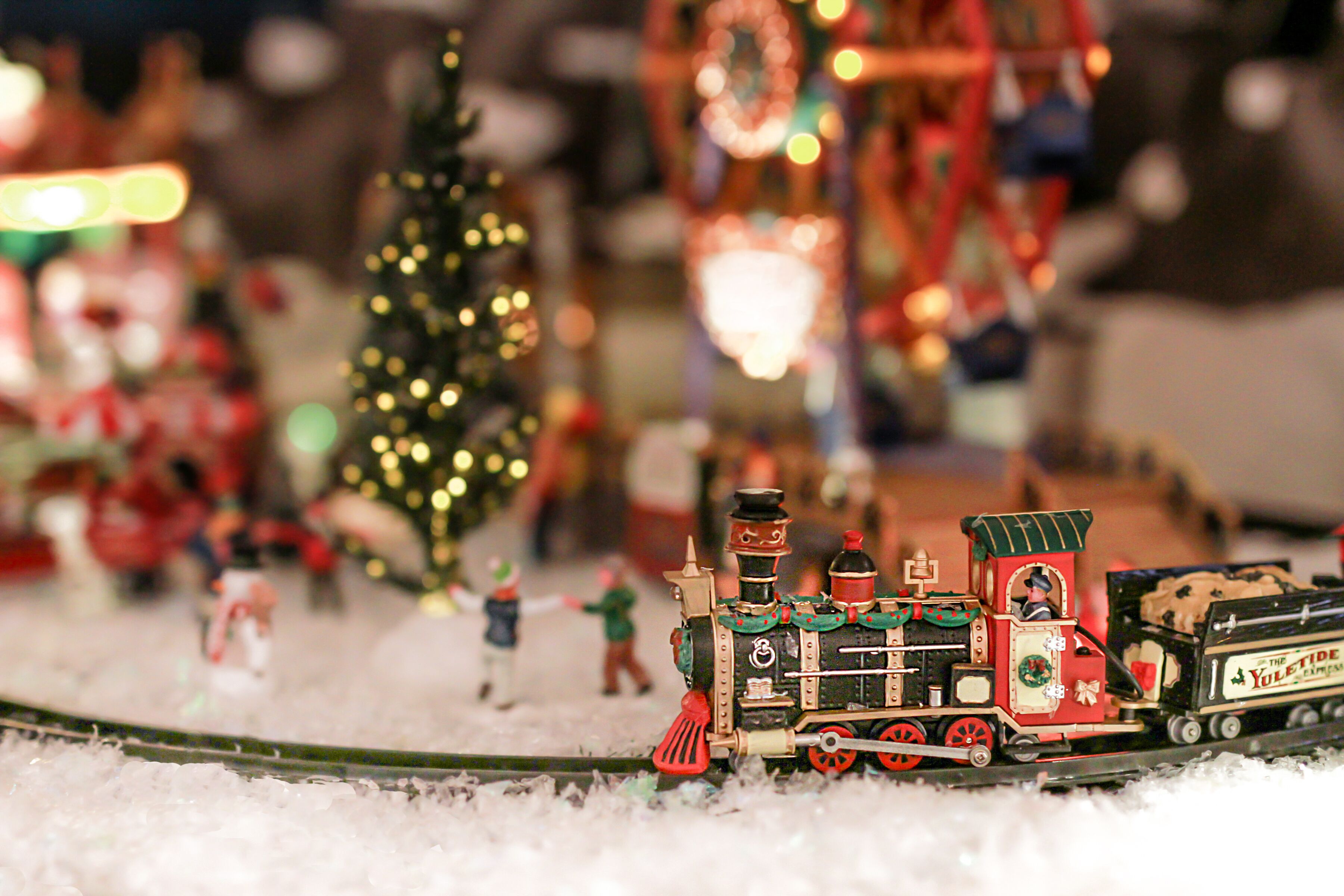 A model train set with a decorated train car and a Christmas tree in the background.