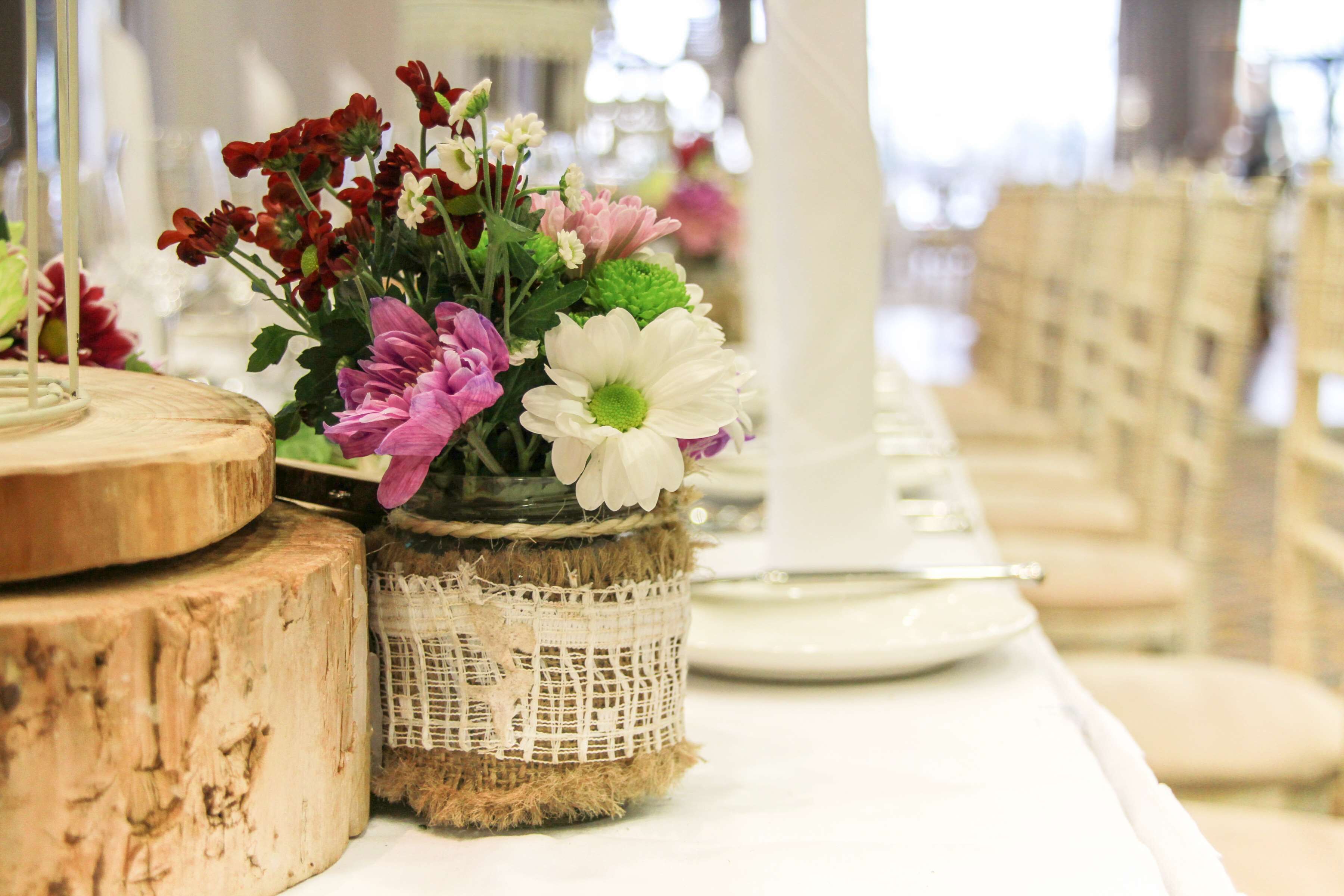 A table setting with a rustic centerpiece featuring a variety of flowers in a burlap-wrapped vase.