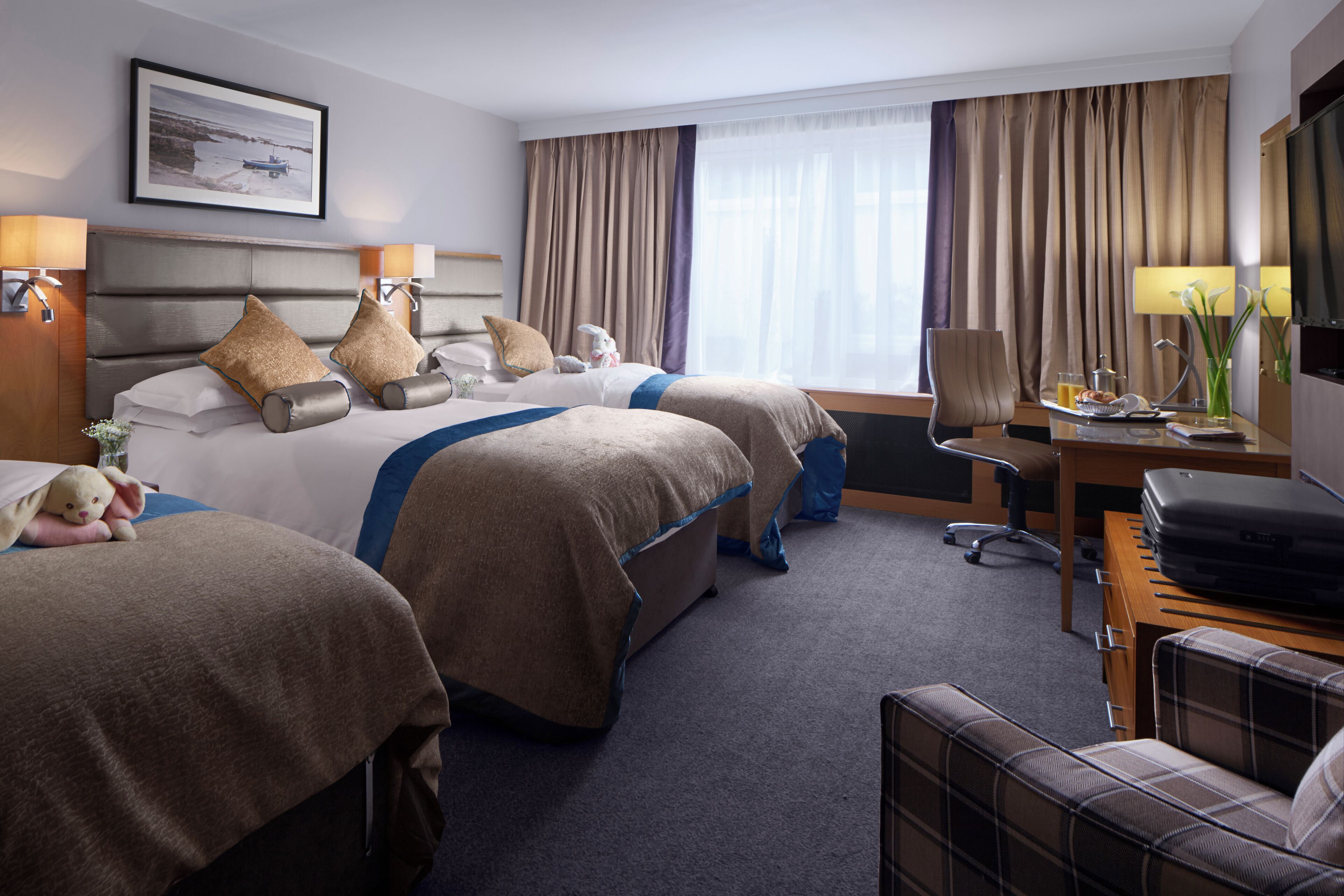 A hotel room with two beds, a desk with a chair, a TV, and a window with curtains.