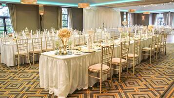 Un salón de banquetes con mesas redondas, manteles blancos y sillas doradas.