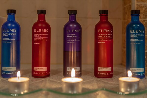 Five bottles of Elemis body oil products with a lit candle in the foreground.