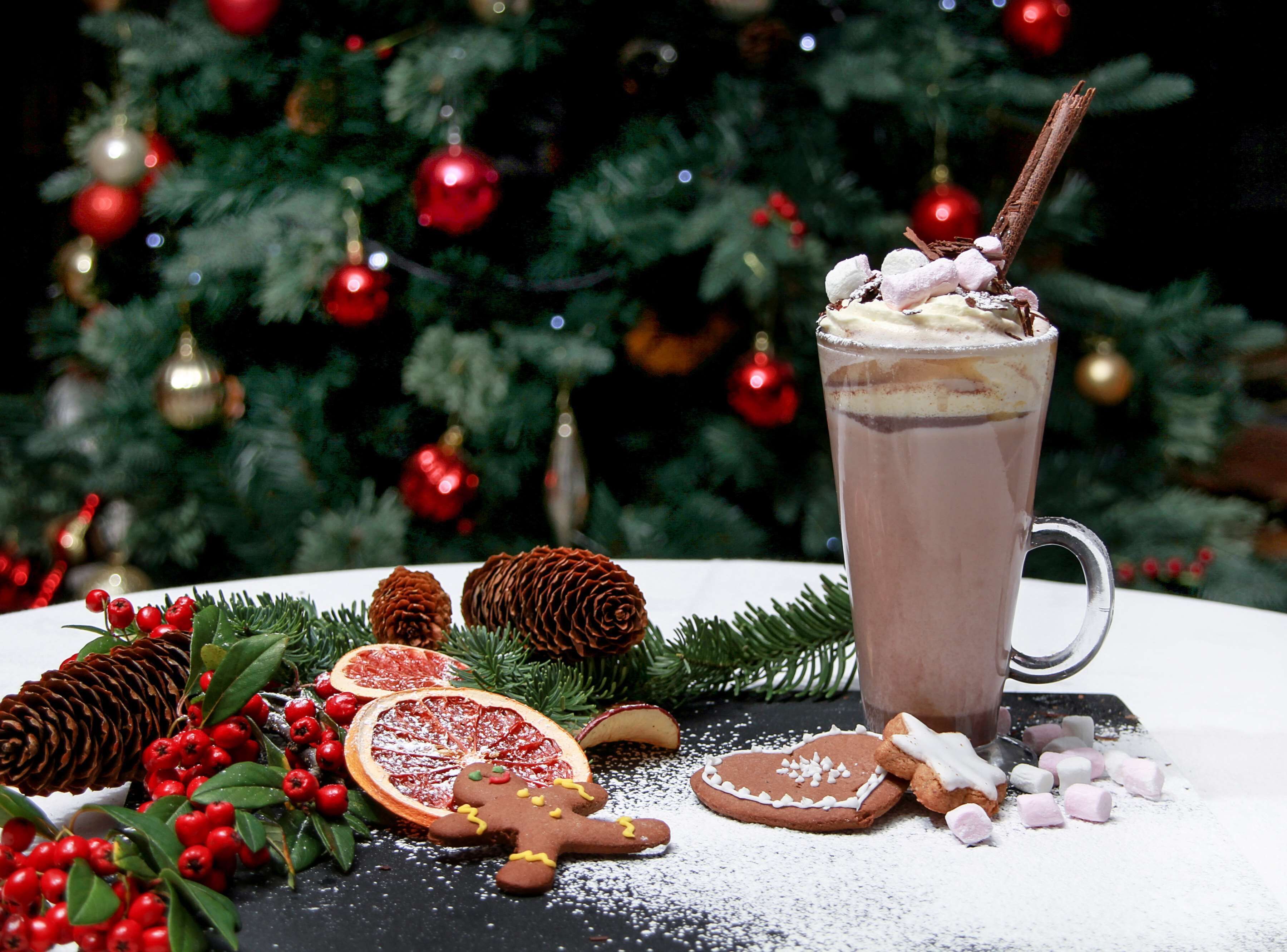 Een feestelijk gedekte tafel met een mok warme chocolademelk, peperkoekjes en kerstdecoraties.