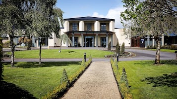 Stunning hotel entrance with a central entrance flanked by double doors, set amidst a beautifully manicured lawn and driveway.