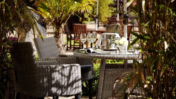 An outdoor dining area with wicker furniture and a table set for two, surrounded by greenery. - Radisson Blu Hotel & Spa, Limerick (Cratloe)