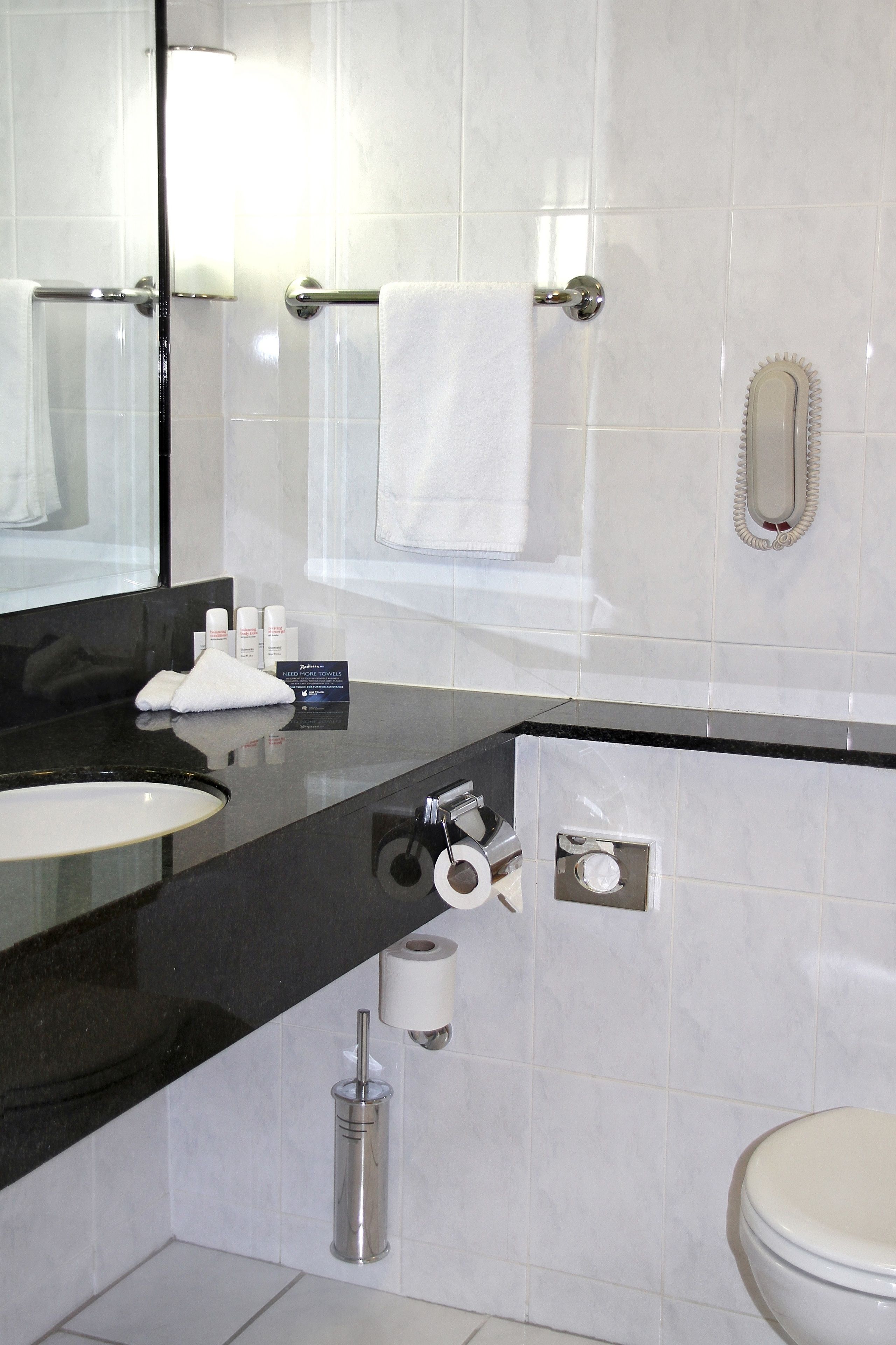 Un baño moderno con encimera negra, lavamanos blanco, espejo, toallero y retrete.