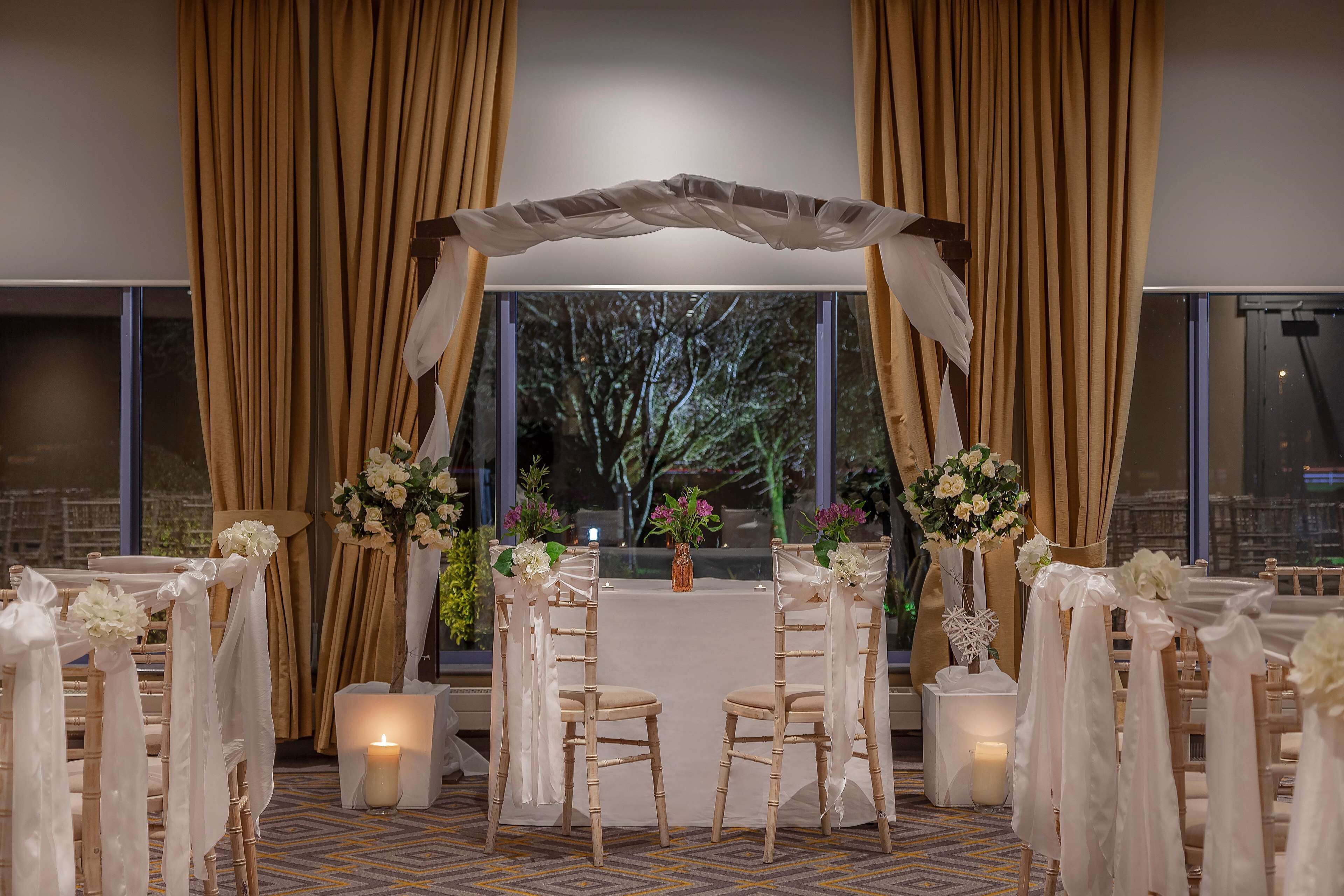 Decoración para una ceremonia de boda, con un arco blanco y adornos florales.