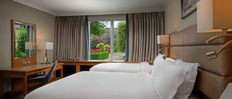Una habitación de hotel con una cama grande, un escritorio, una silla, un espejo y una ventana con cortinas.