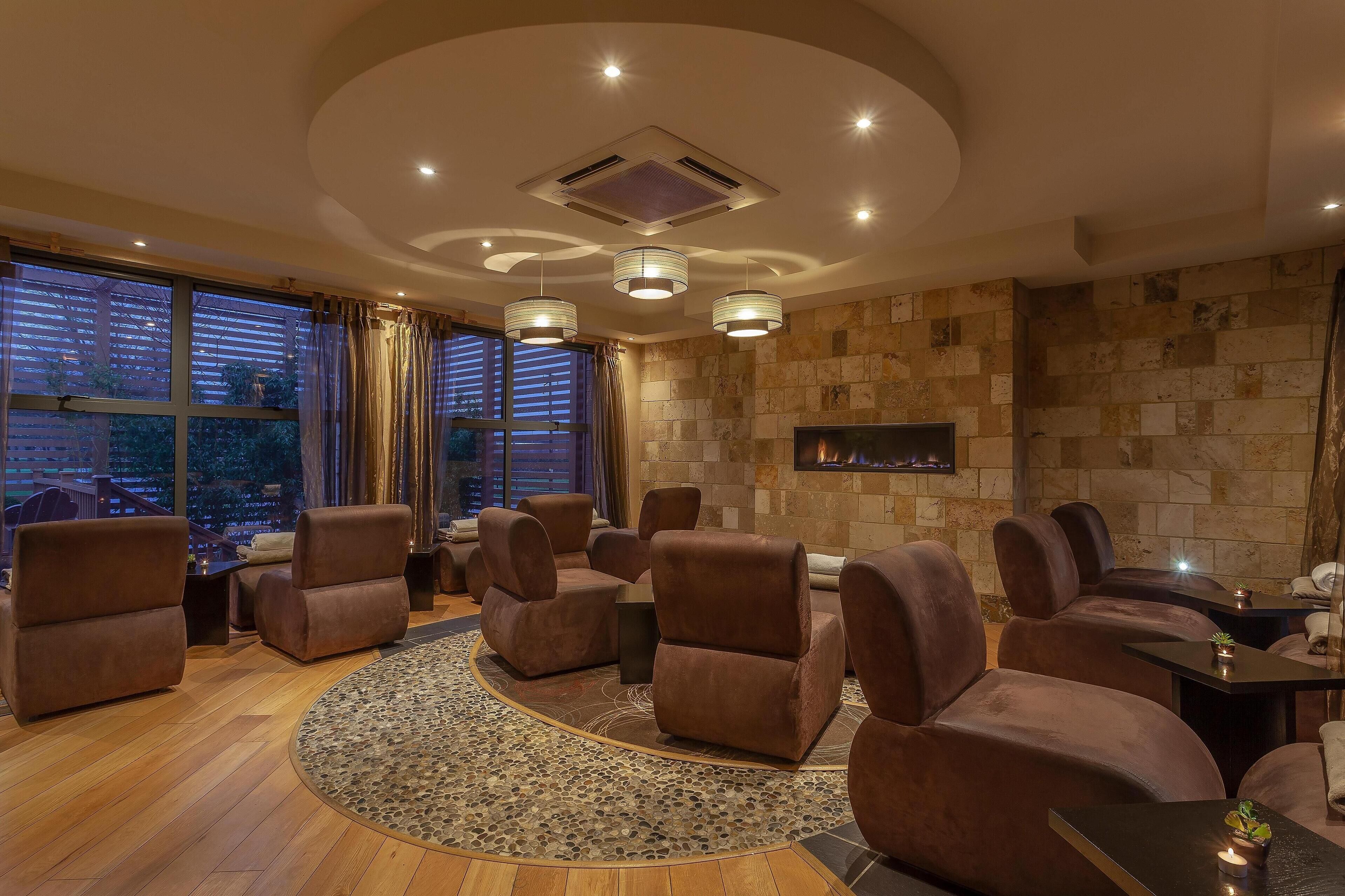 A modern lounge area with leather sofas, a fireplace, and large windows with curtains.