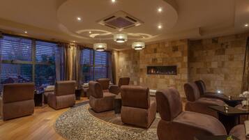 A modern lounge area with leather sofas, a fireplace, and large windows with curtains.