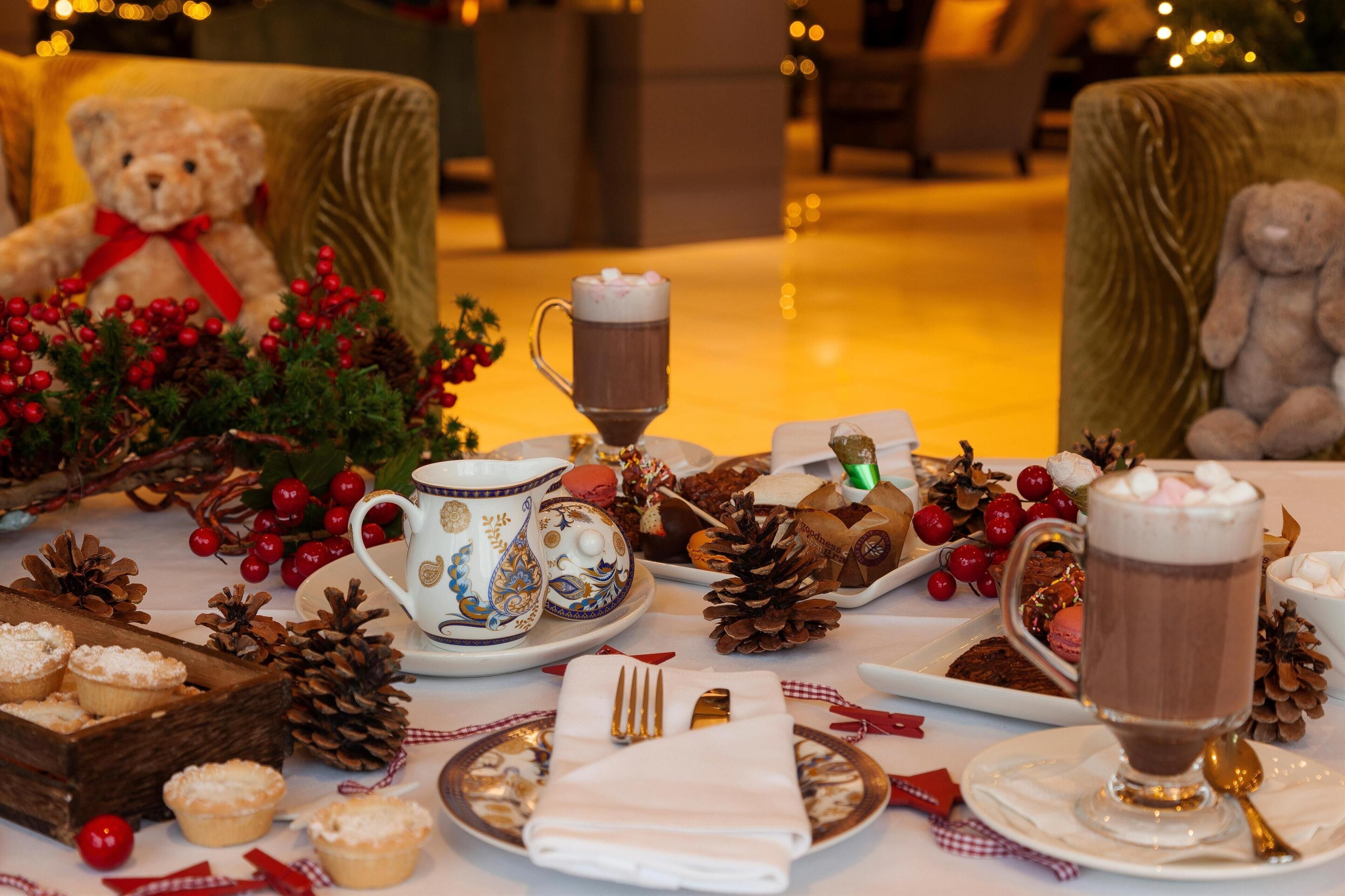 A table set with a teapot, mugs, pastries, and a teddy bear.