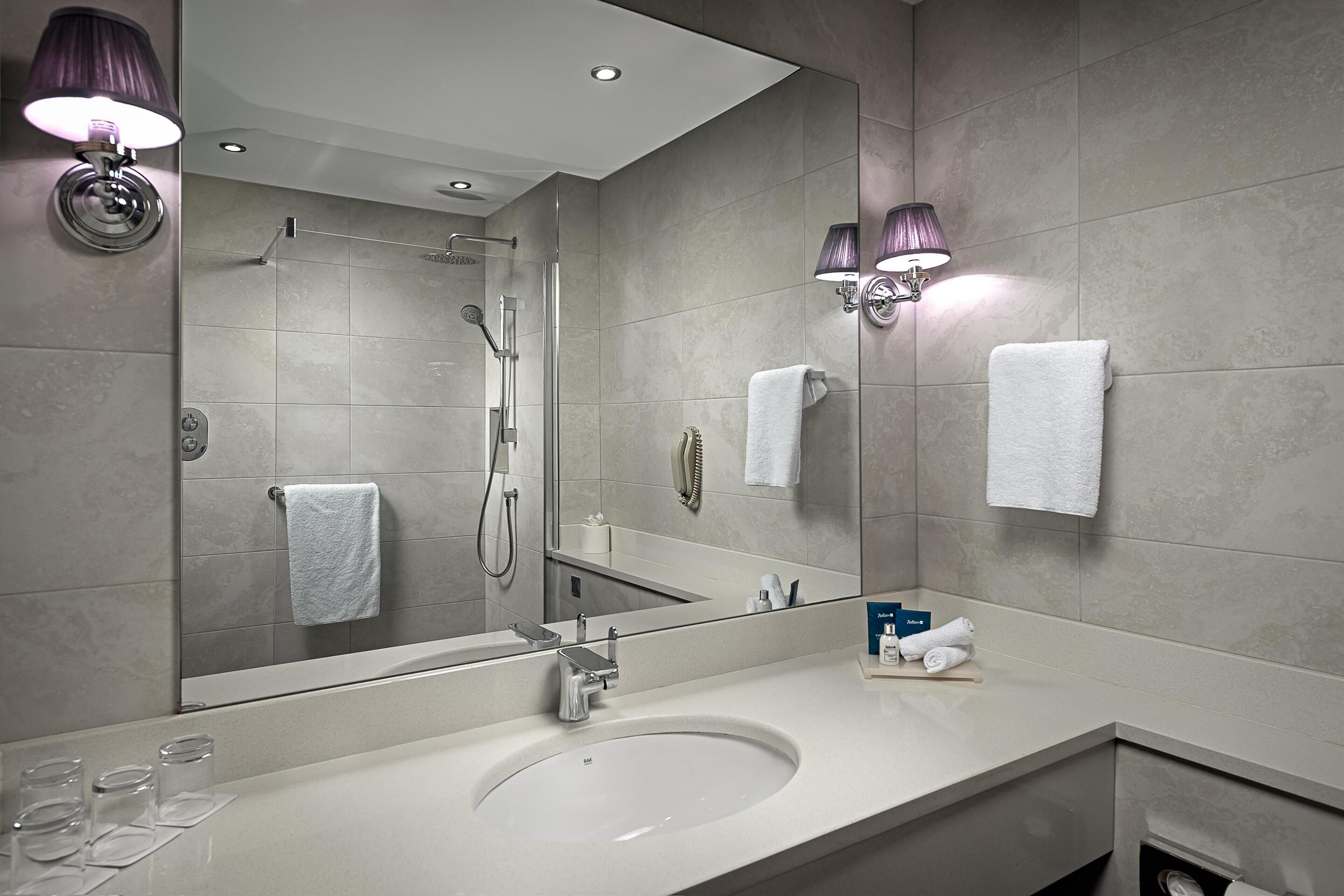 A modern bathroom with a large mirror, a sink, and a shower.