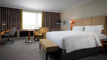 Une chambre d’hôtel avec un grand lit, un bureau avec une chaise, une petite table et un banc.