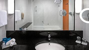 A modern bathroom with a black granite countertop, a white sink, a glass shower enclosure, and a wooden door.
