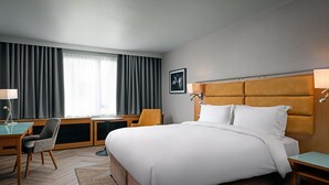 A hotel room with a large bed, a desk, a chair, and a window with curtains.