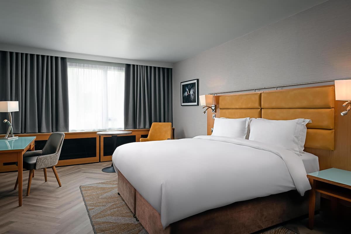 A hotel room with a large bed, a desk, a chair, and a window with curtains.