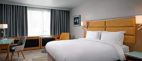 Una habitación de hotel con una cama grande, un escritorio, una silla y un ventanal con cortinas.