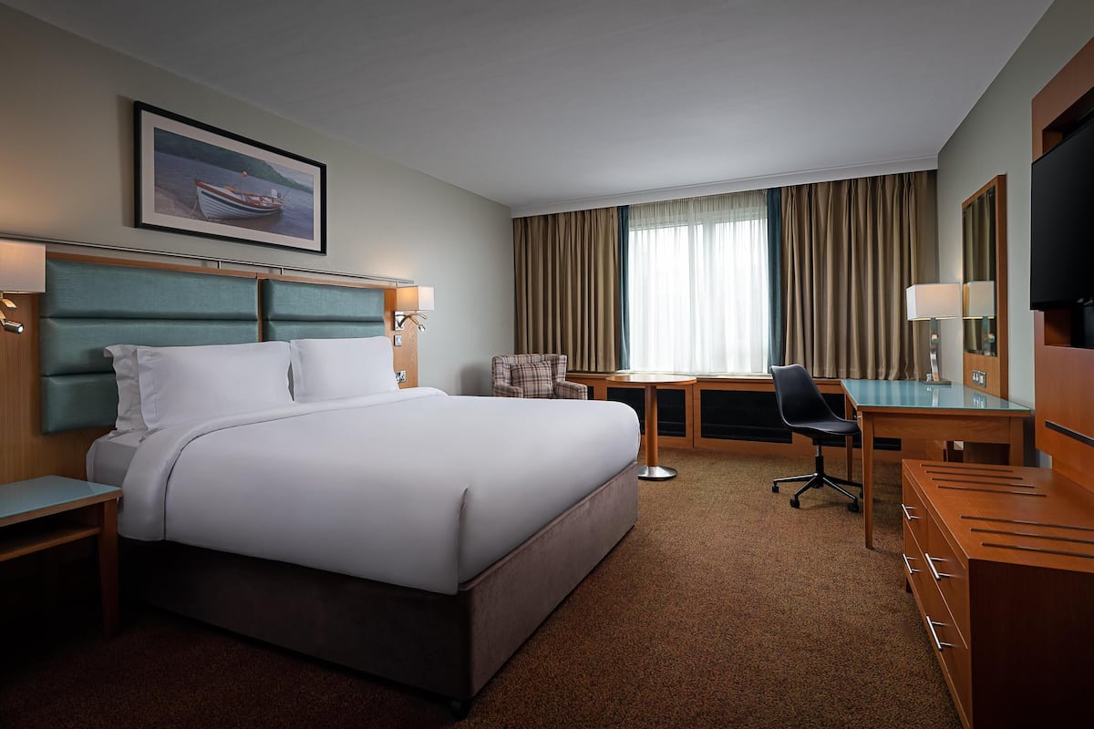 A hotel room with a bed, desk, chair, and a television.