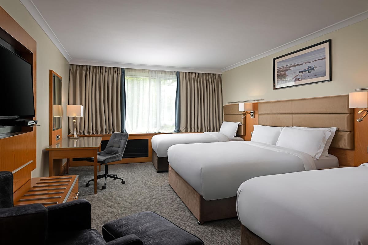A hotel room with two beds, a desk, a chair, a TV, and a window with curtains.