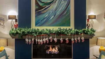 Une cheminée ornée de guirlandes, un sapin de Noël et un grand tableau abstrait accroché au-dessus.