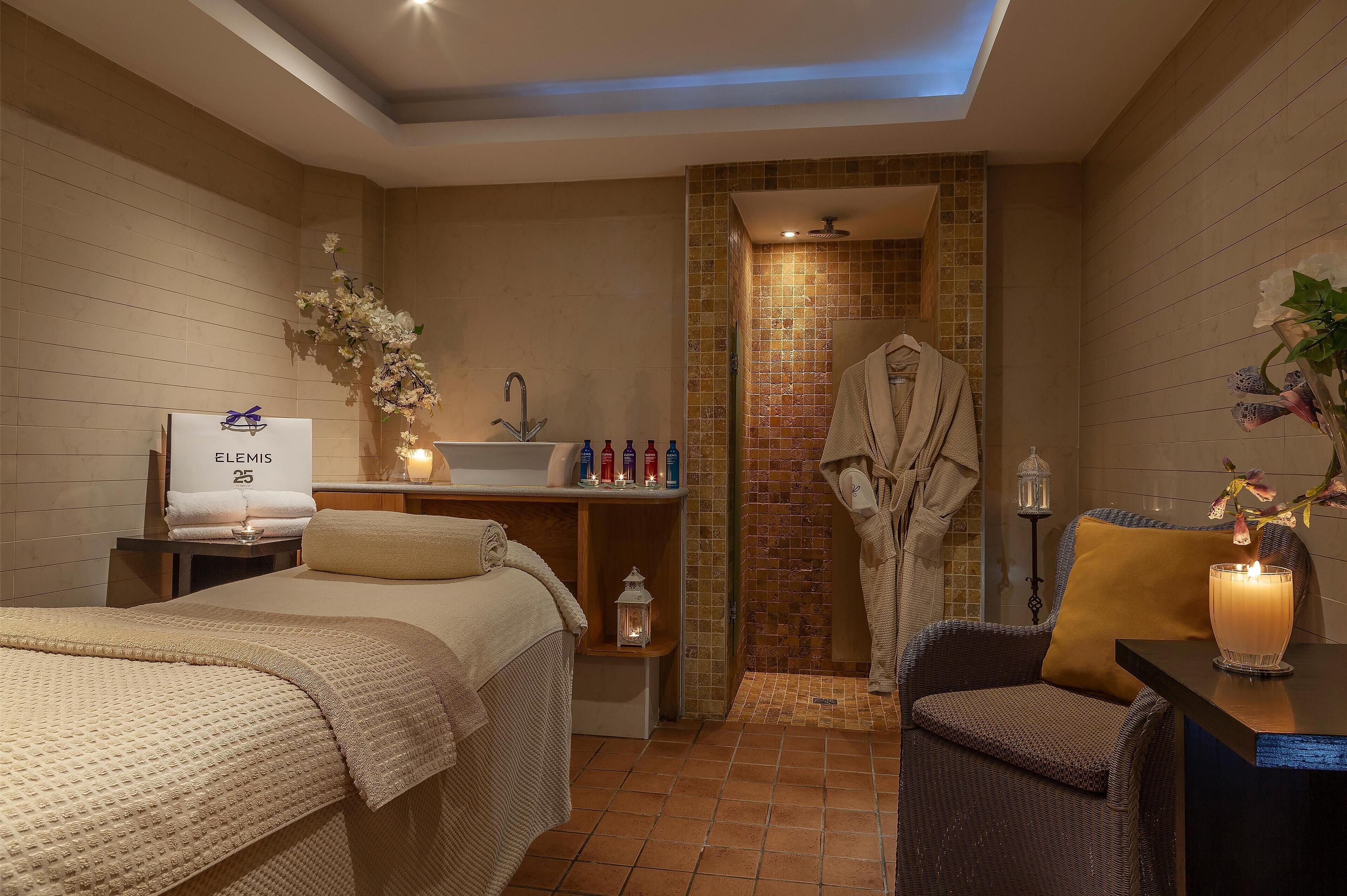 A hotel room with a bed, a small table with toiletries, a robe hanging, and a shower area.