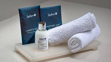 Et badeværelsesbord med et hvidt håndklæde, en flaske Radisson-kropslotion og to blå badehuetasker.