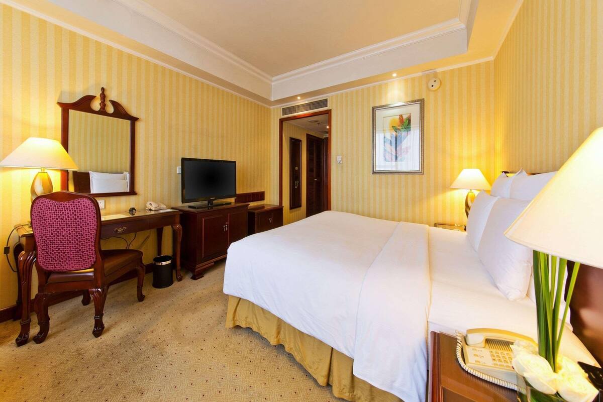 A hotel room with a bed, desk, chair, television, and lamps.