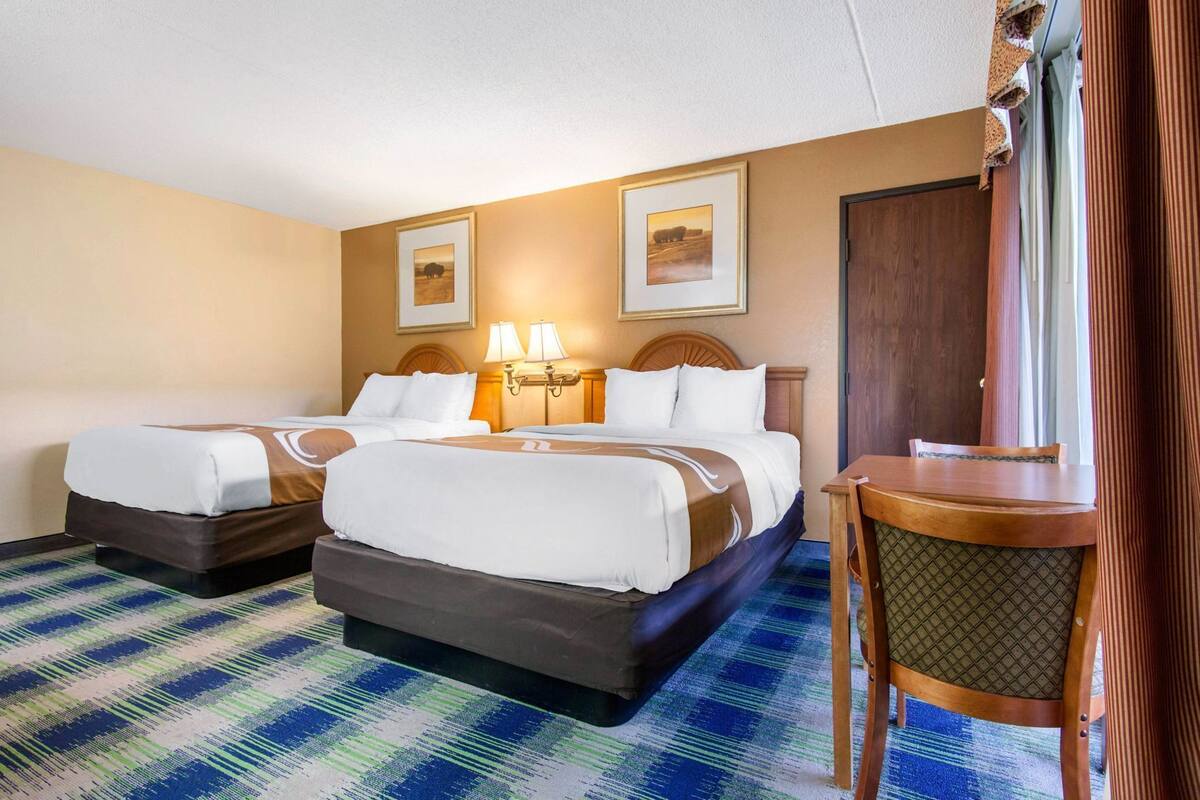 Quarto de hotel com duas camas, uma escrivaninha e uma cadeira.
