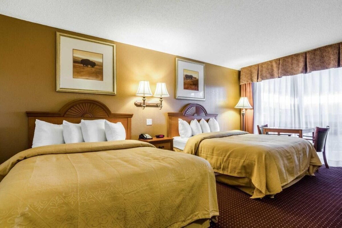 Habitación de hotel con dos camas, un escritorio, una silla y dos lámparas de pared.