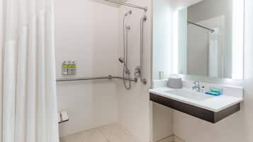 A modern bathroom with a walk-in shower, grab bars, a white sink with a dark countertop, and a mirror above the sink.