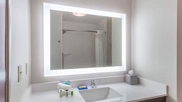 A bathroom with a large mirror, a sink, and a shower.