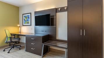 A modern hotel room with a dark wood desk, a flat-screen TV, a green chair, and a large wardrobe.