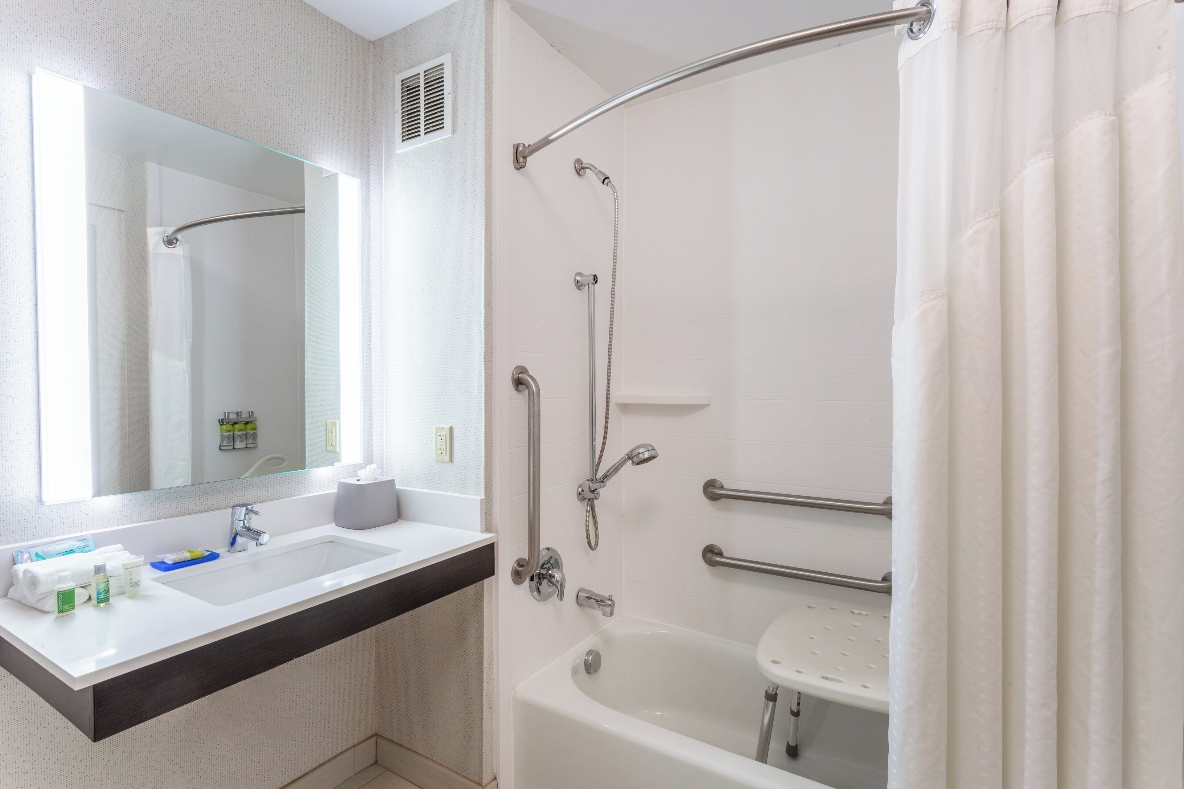 Un baño moderno con lavamanos, espejo y bañera blancos.