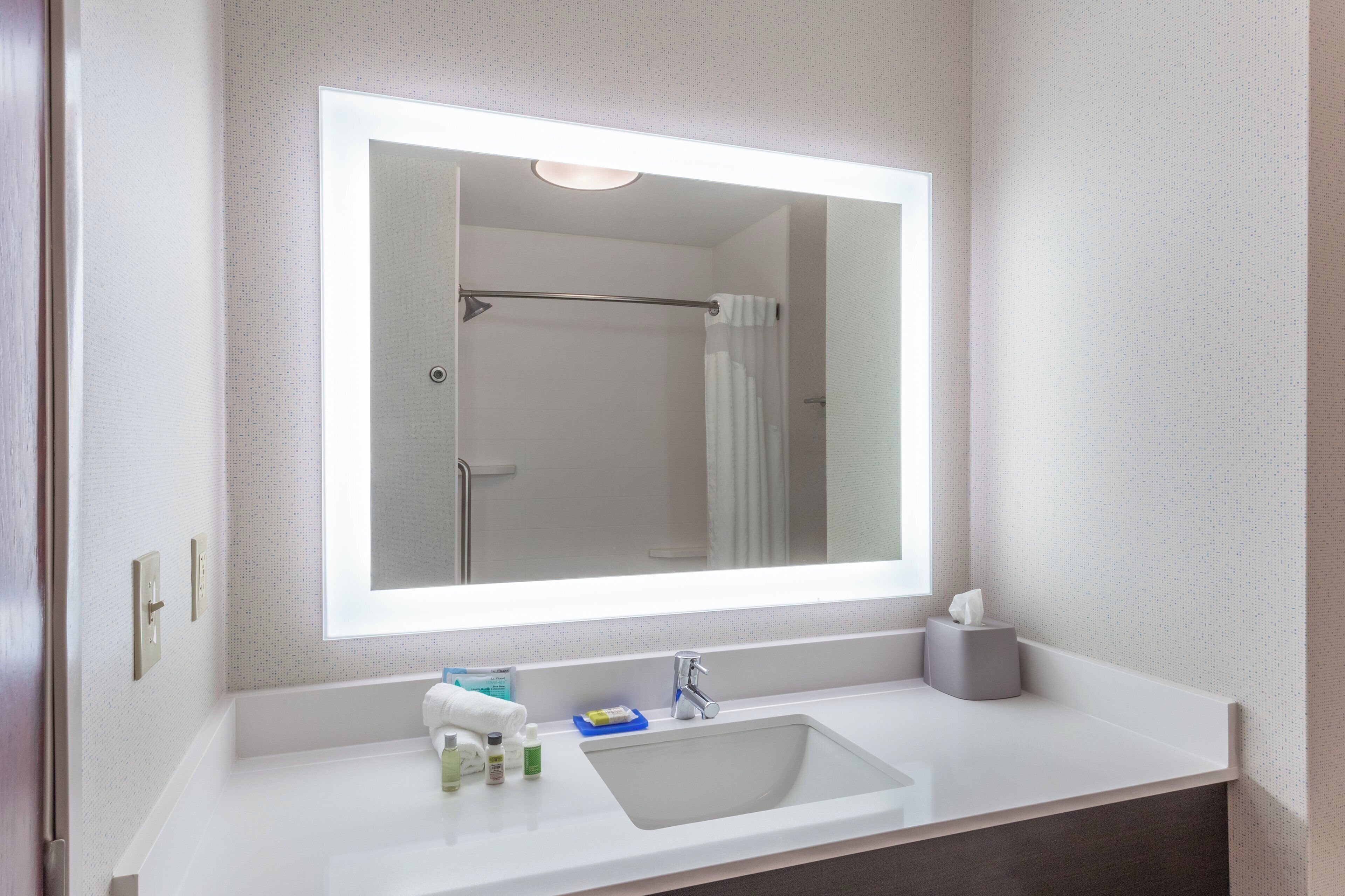 A bathroom with a large mirror, a sink, a towel, and toiletries.