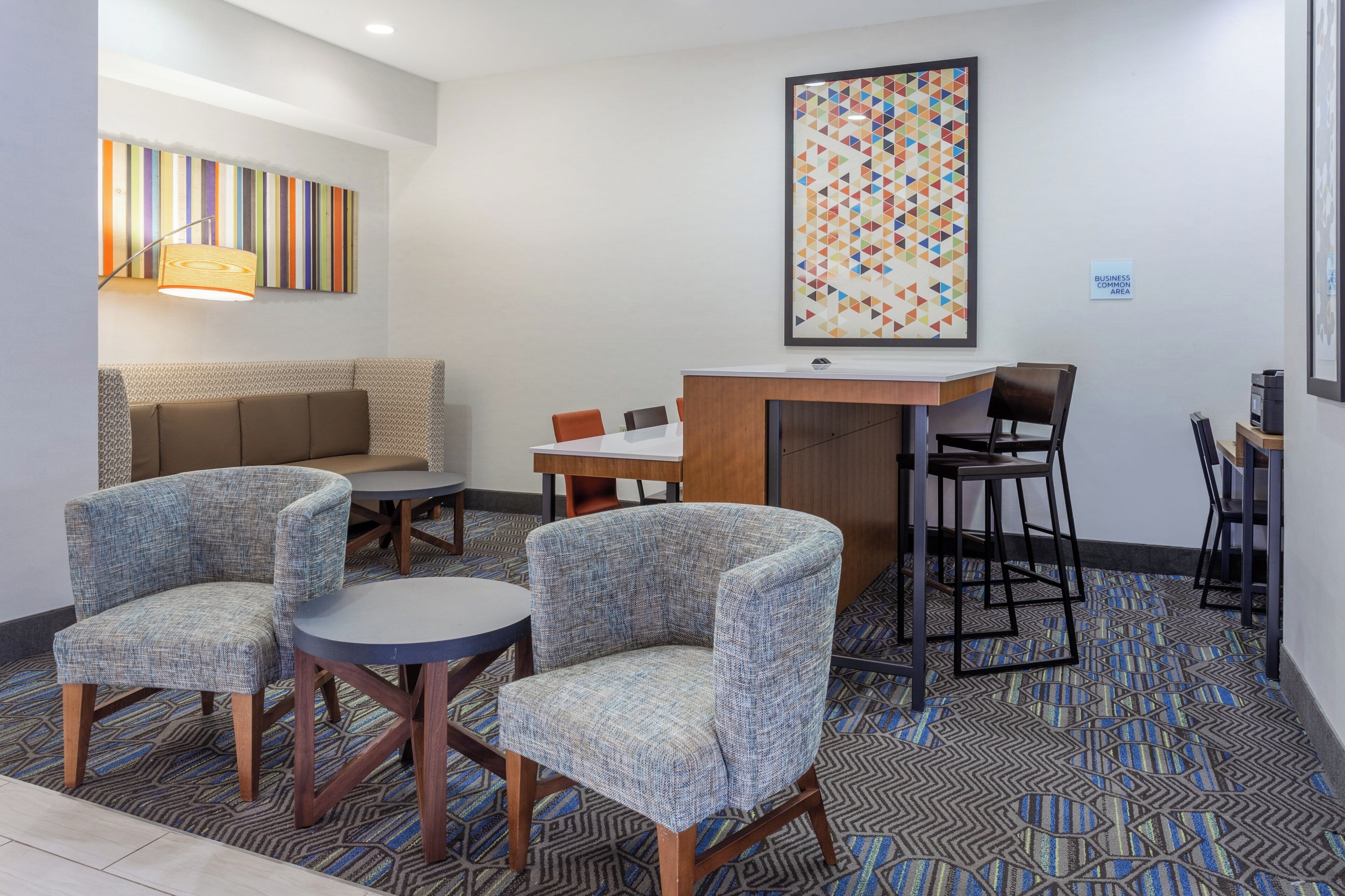 Un hall de hotel con un sofá, dos sillones, una mesita, una zona de bar y una obra de arte enmarcada en la pared.