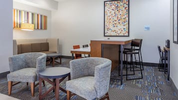 Un hall de hotel con un sofá, dos sillones, una mesita, una zona de bar y una obra de arte enmarcada en la pared.