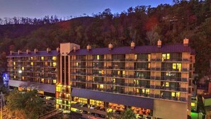 Un hotel de varios pisos con balcones, una zona de estacionamiento techada y vistas al bosque circundante.
