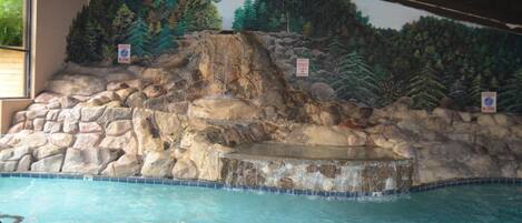 A pool with a rocky waterfall feature and a mural of a forested landscape.