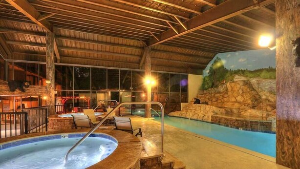 Una piscina interior con un jacuzzi, paredes de piedra y un mural de un paisaje natural.