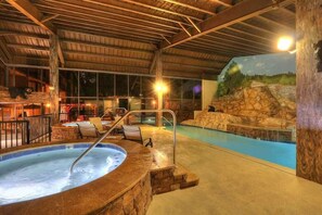 Une piscine intérieure dotée d’un jacuzzi, de murs en pierre et d’une fresque représentant un paysage naturel.