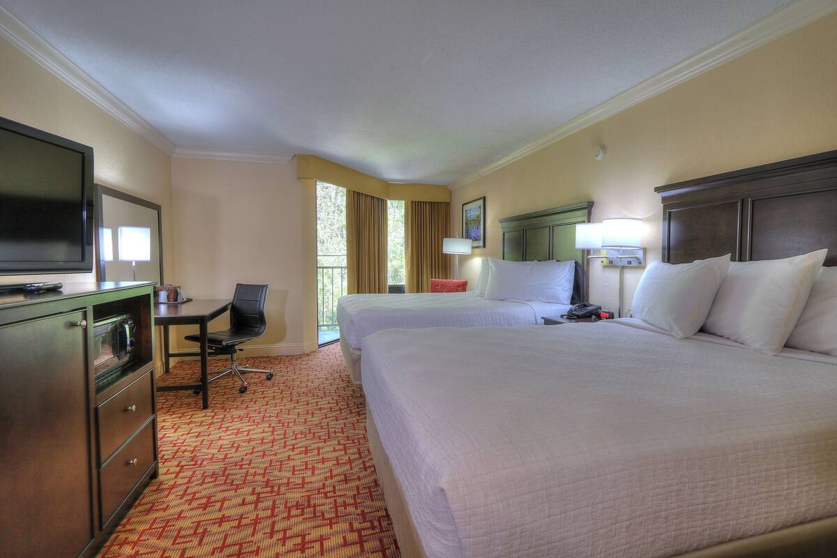 A hotel room with two beds, a desk with a chair, a television, and a window with curtains.