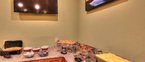 A buffet setup with various food items and a television mounted on the wall.