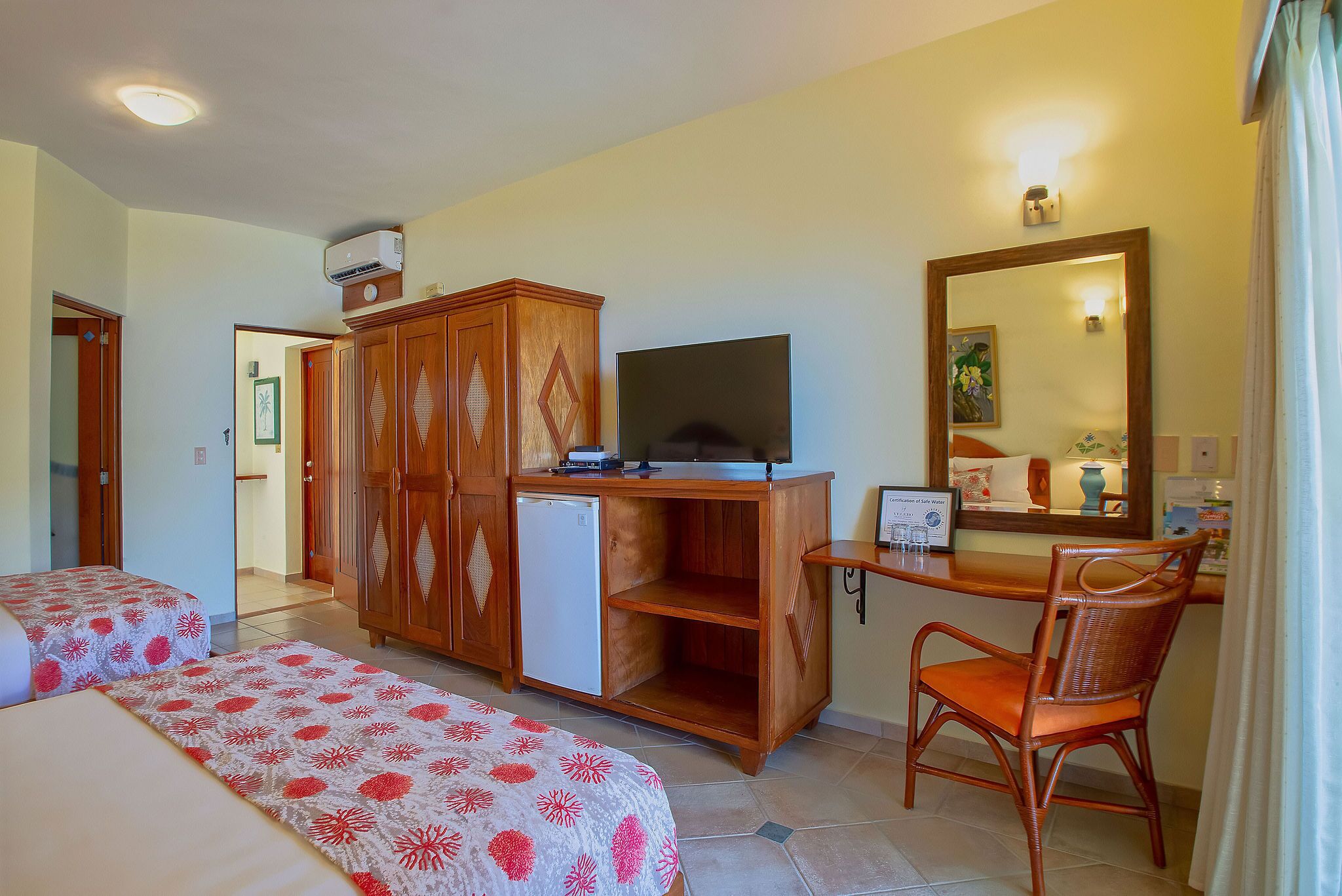 Habitación de hotel con dos camas, un escritorio con televisor, un refrigerador pequeño, un armario de madera y un espejo.