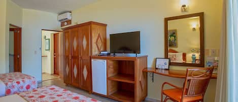 Habitación de hotel con dos camas, un escritorio con televisor, un refrigerador pequeño, un armario de madera y un espejo.