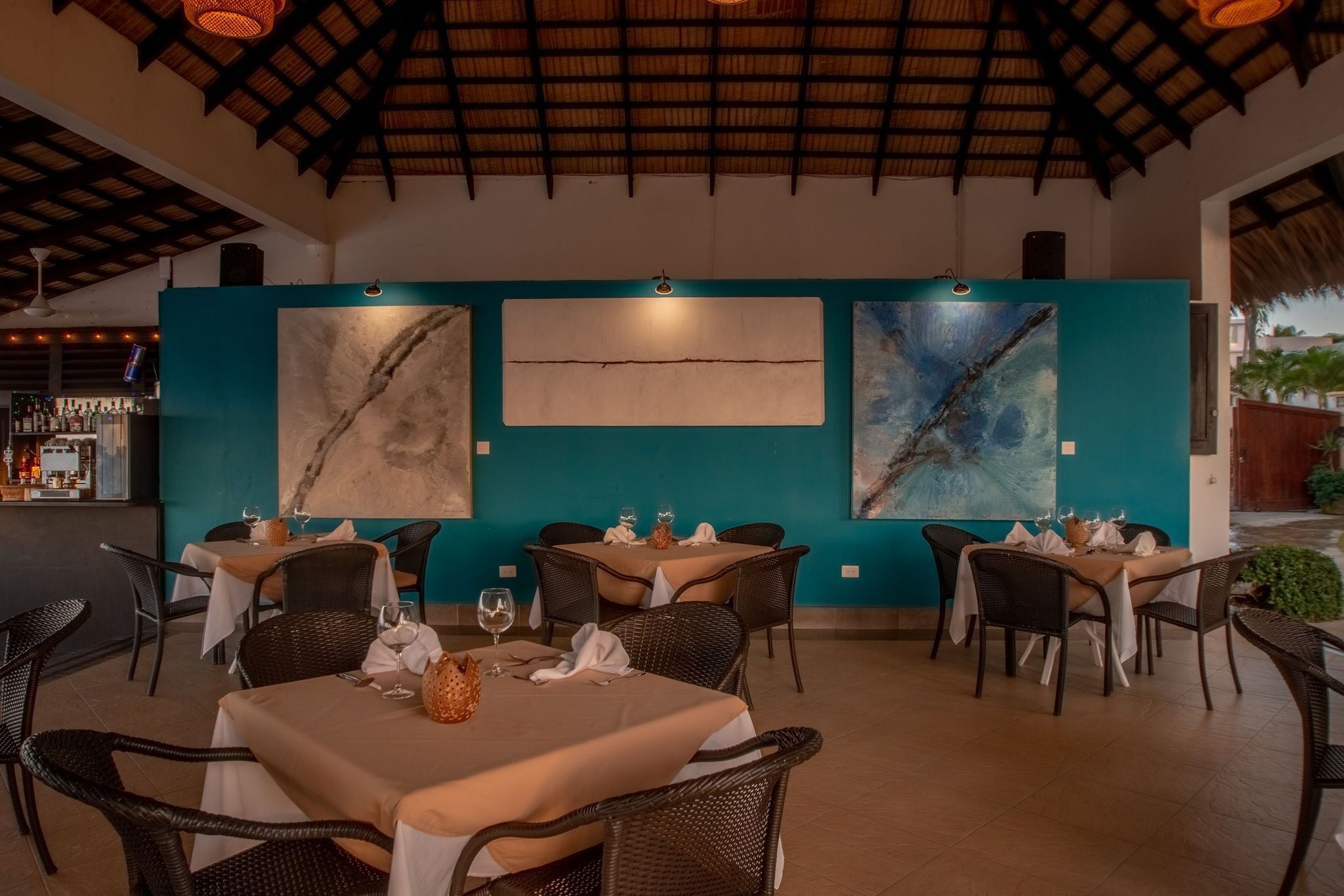 An outdoor dining area with tables and chairs, a bar in the background, and artwork on the walls.