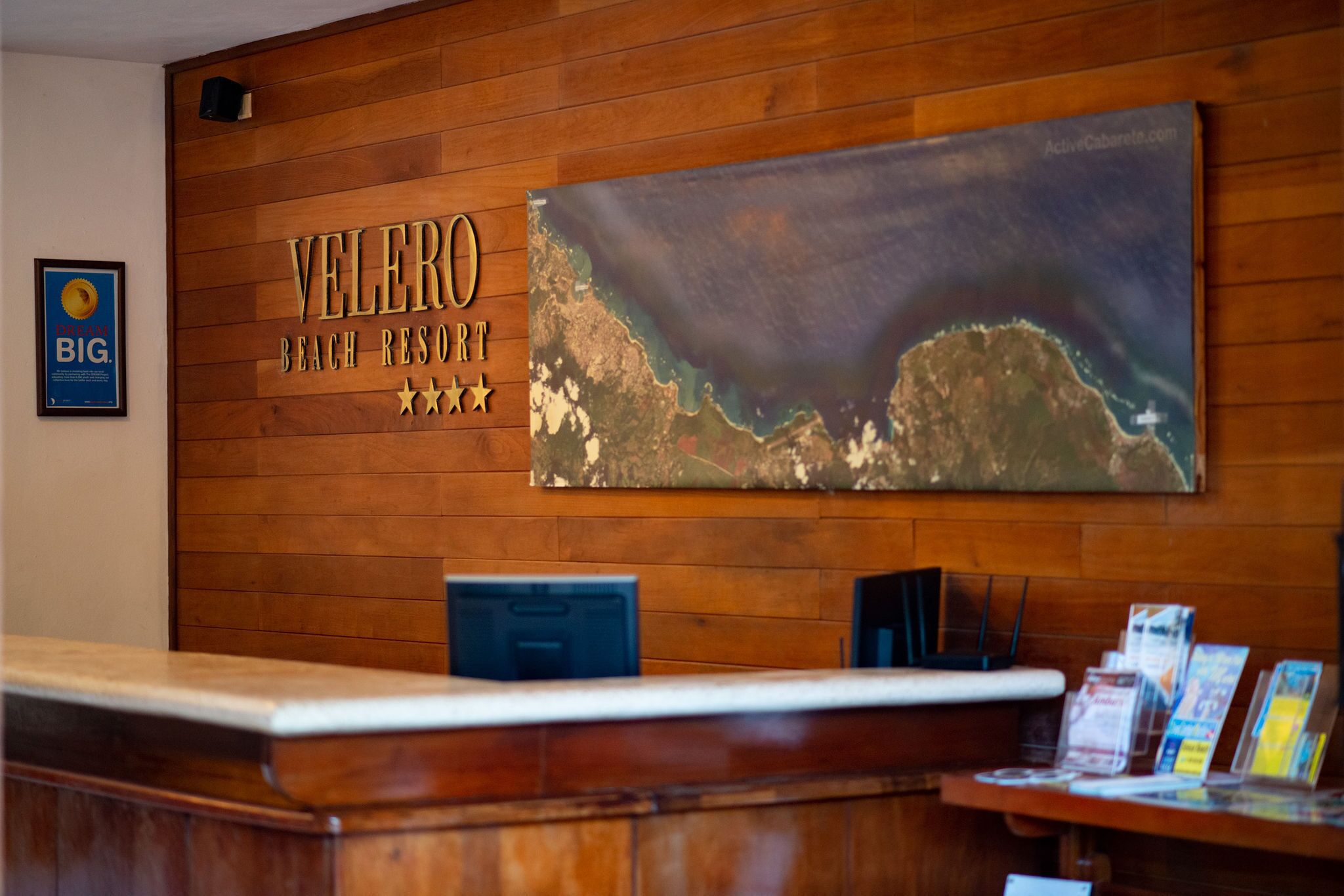 A wooden reception desk with a large sign reading "VELERO BEACH RESORT" and a map of the resort.