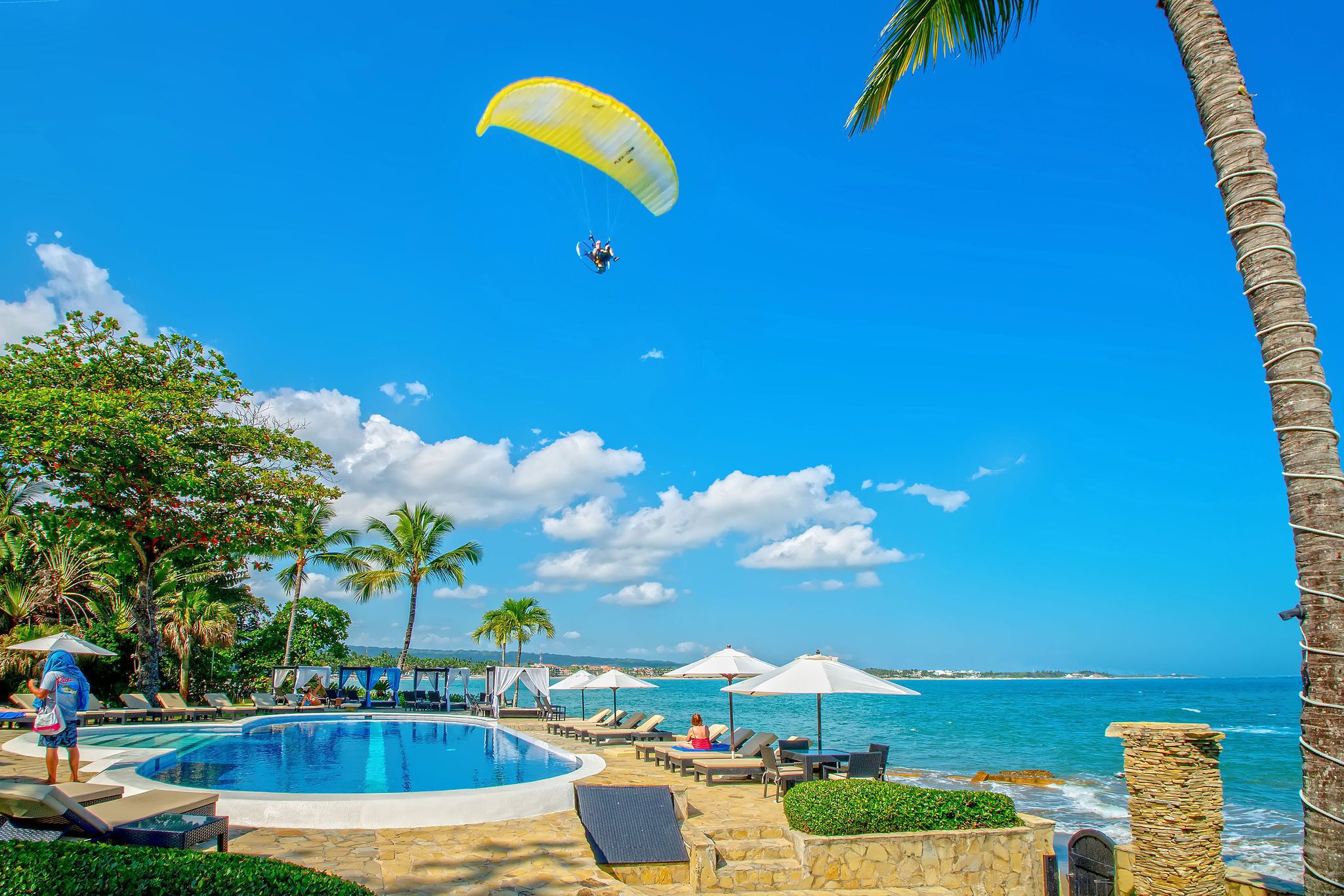 A poolside area with lounge chairs, umbrellas, and a parasail in the background.